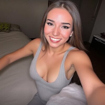 Smiling woman taking a selfie in a gray tank top in a bedroom.