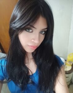Close-up portrait of a woman with long dark hair, blue eyes, and a blue top, looking at the camera.